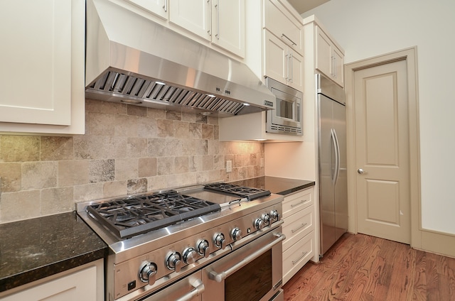 kitchen featuring backsplash, built in appliances, light hardwood / wood-style flooring, dark stone countertops, and white cabinetry