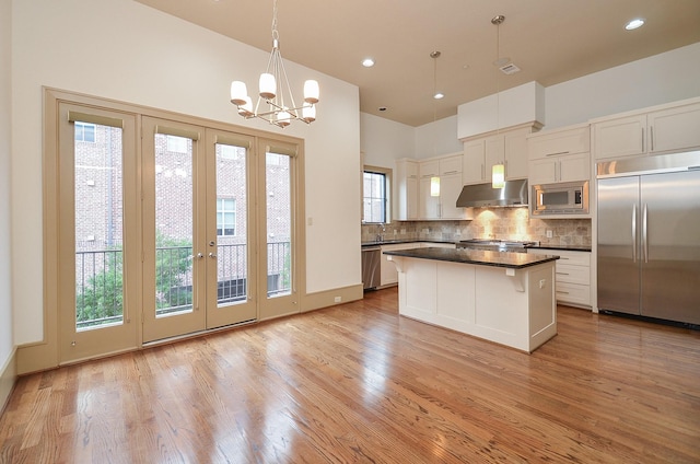 kitchen with built in appliances, pendant lighting, white cabinetry, and extractor fan