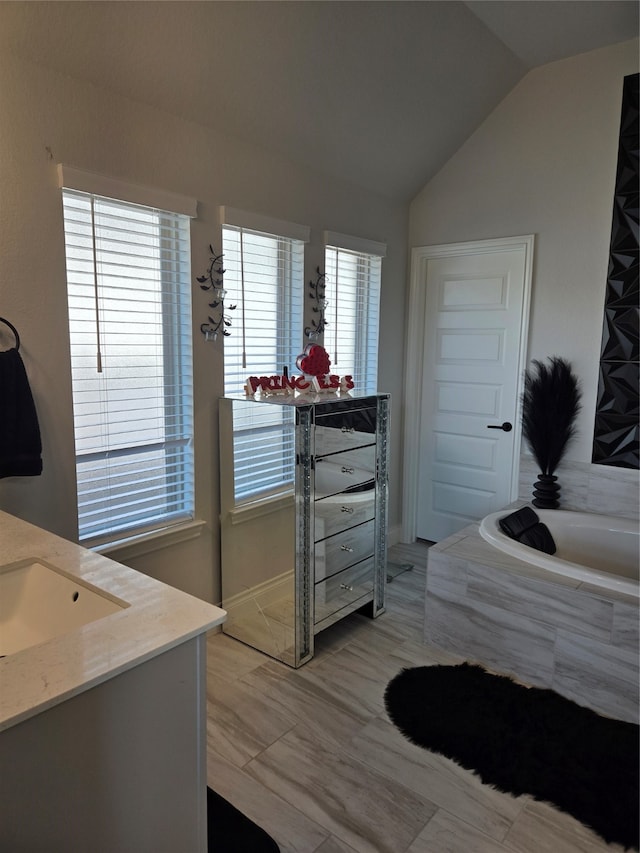 bathroom featuring vanity, a relaxing tiled tub, vaulted ceiling, and a healthy amount of sunlight