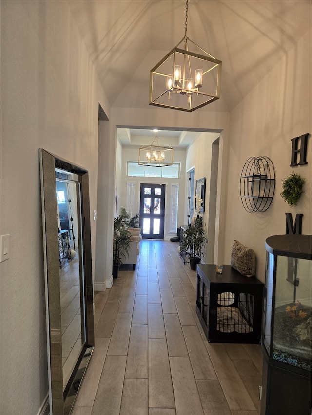 hallway with hardwood / wood-style floors, high vaulted ceiling, and an inviting chandelier