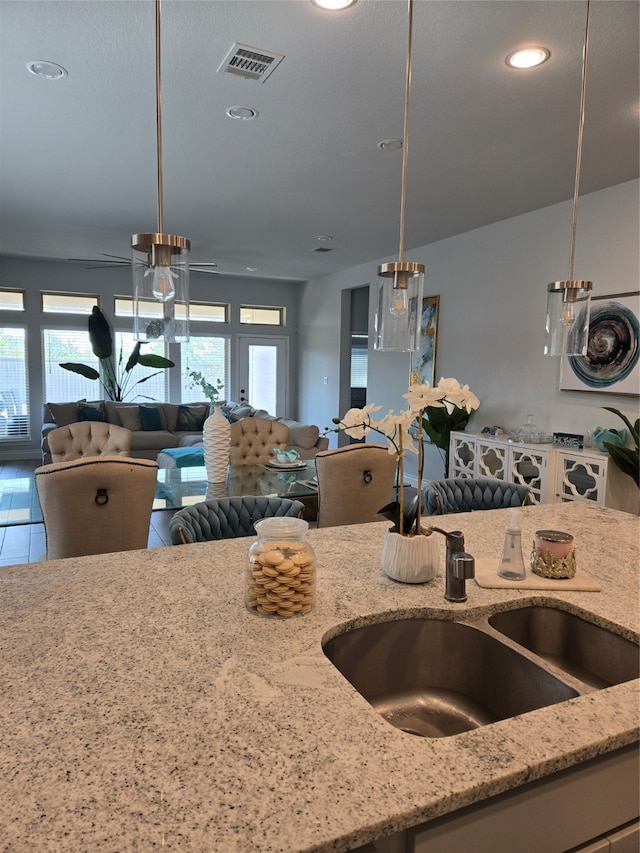 kitchen featuring tile patterned flooring, decorative light fixtures, light stone counters, and sink