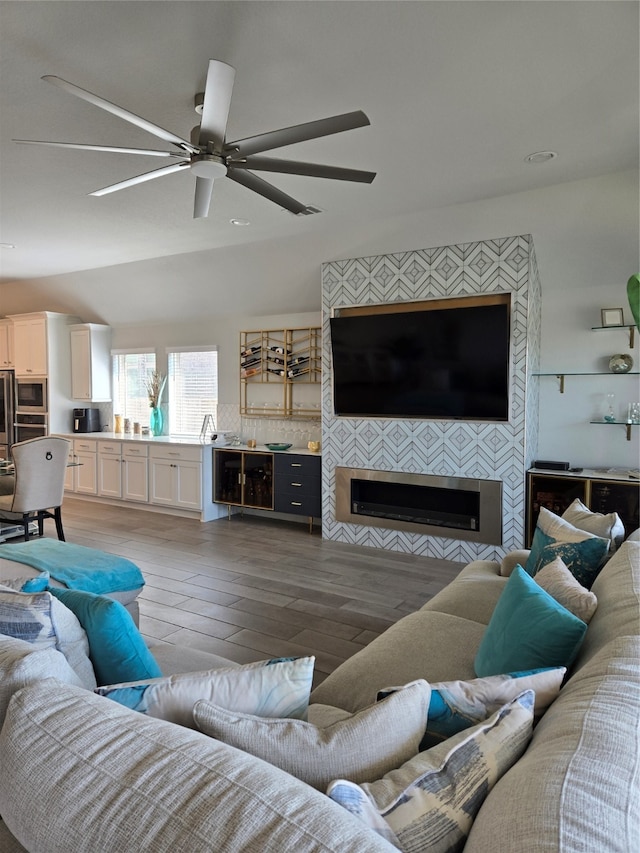 living room with hardwood / wood-style flooring, ceiling fan, and a tiled fireplace