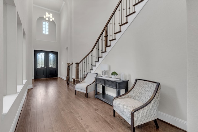 entryway featuring french doors, a high ceiling, a notable chandelier, crown molding, and hardwood / wood-style flooring