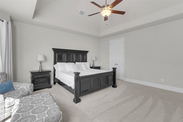 carpeted bedroom with a raised ceiling, ceiling fan, and a closet