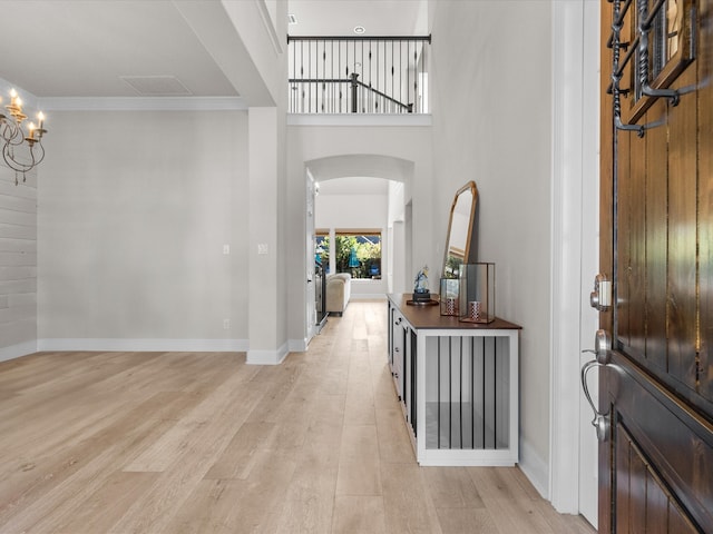 foyer entrance featuring a high ceiling, light hardwood / wood-style floors, ornamental molding, and a notable chandelier