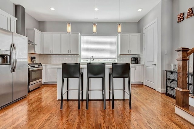 kitchen with a center island, hanging light fixtures, light hardwood / wood-style flooring, white cabinets, and appliances with stainless steel finishes