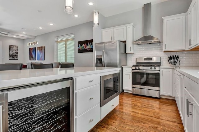 kitchen featuring light wood-type flooring, wall chimney exhaust hood, stainless steel appliances, beverage cooler, and white cabinetry