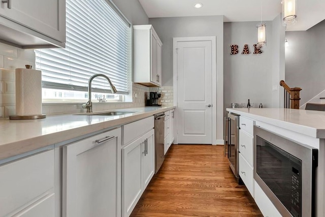 kitchen with white cabinets, hanging light fixtures, sink, light hardwood / wood-style flooring, and appliances with stainless steel finishes