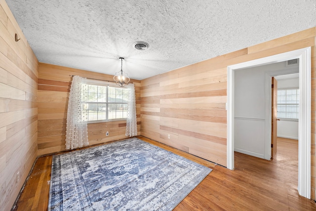 unfurnished dining area with a textured ceiling, hardwood / wood-style flooring, an inviting chandelier, and wood walls