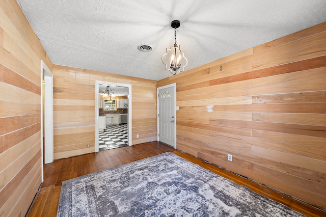 empty room with a textured ceiling, dark hardwood / wood-style flooring, a notable chandelier, and wood walls