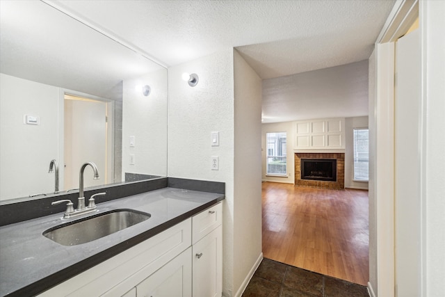 kitchen with a fireplace, a textured ceiling, sink, white cabinets, and dark hardwood / wood-style floors