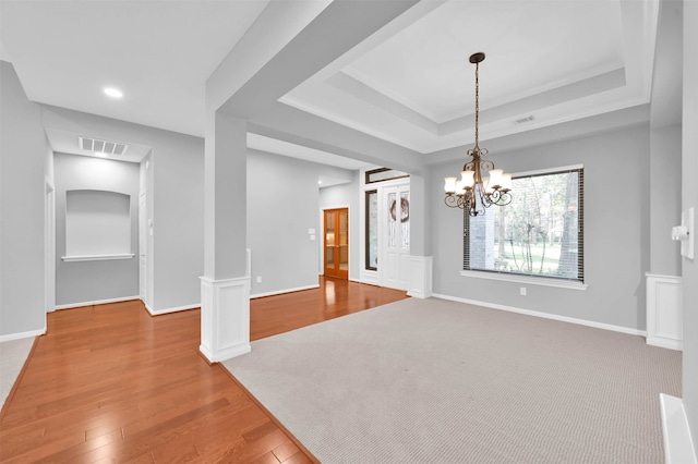 empty room featuring wood-type flooring, decorative columns, a tray ceiling, and a notable chandelier