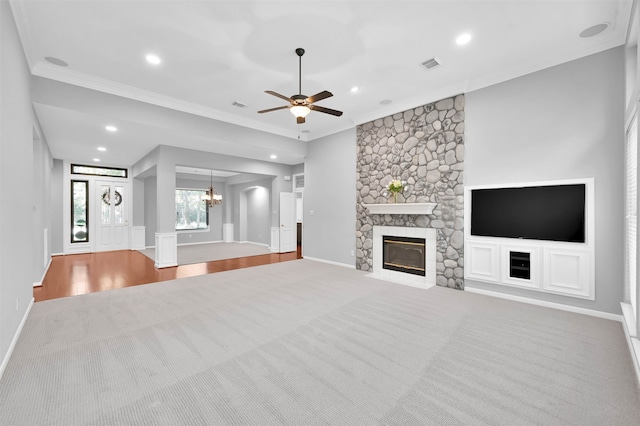 unfurnished living room with wood-type flooring, ceiling fan with notable chandelier, a stone fireplace, and ornamental molding