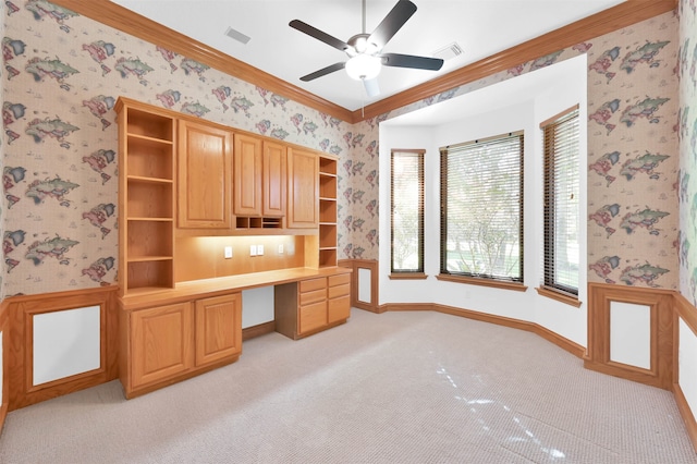 unfurnished office with built in desk, light colored carpet, ceiling fan, and ornamental molding