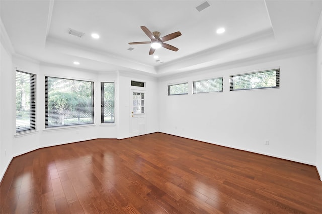 empty room featuring a tray ceiling, wood-type flooring, and ornamental molding