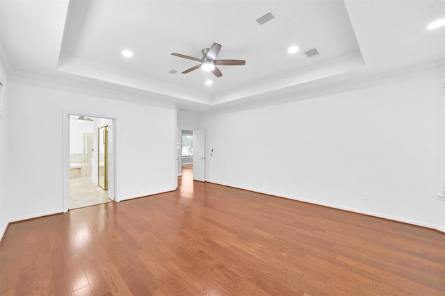 unfurnished bedroom with hardwood / wood-style floors, a tray ceiling, and ensuite bath