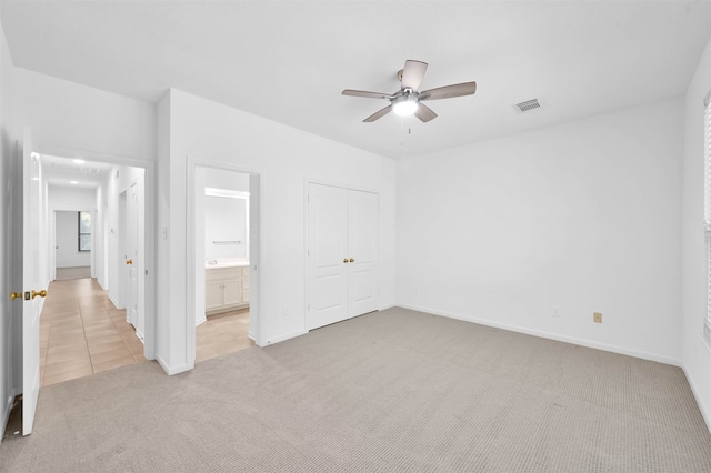 unfurnished bedroom with a closet, light colored carpet, ceiling fan, and connected bathroom