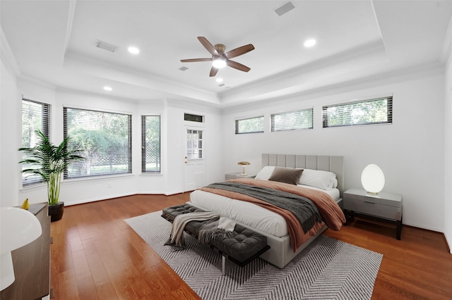 bedroom with ceiling fan, ornamental molding, dark wood-type flooring, and a tray ceiling