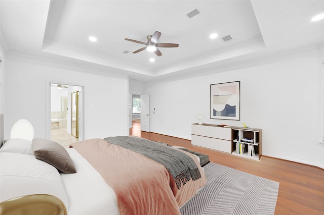 bedroom with wood-type flooring, ensuite bath, a raised ceiling, and ceiling fan