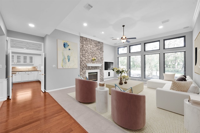 living room featuring crown molding, ceiling fan, a fireplace, and wood-type flooring