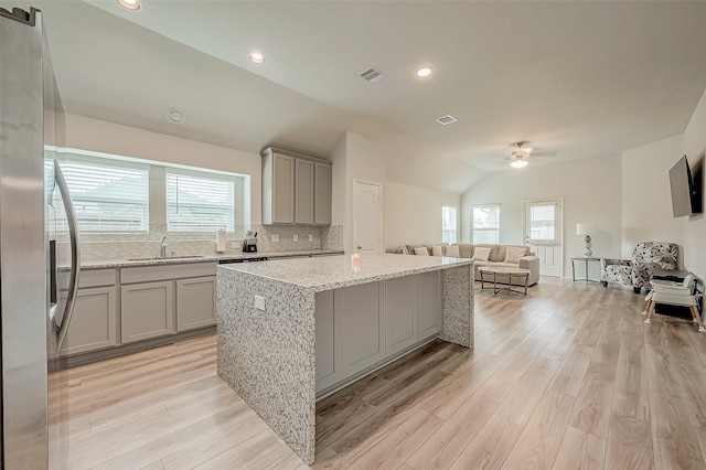 kitchen featuring vaulted ceiling, stainless steel fridge, light hardwood / wood-style floors, a kitchen island, and light stone counters