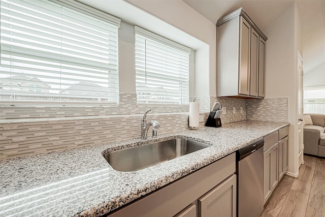 kitchen with dishwasher, light stone counters, sink, and light hardwood / wood-style flooring