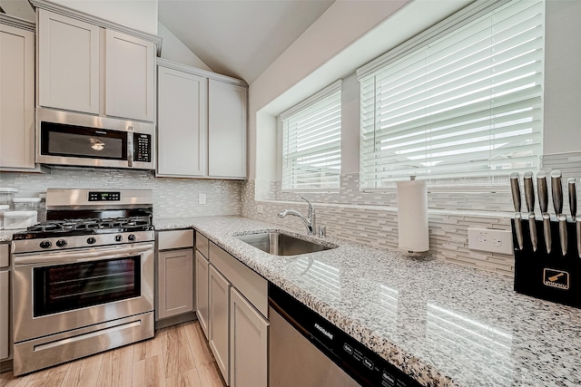 kitchen featuring backsplash, sink, vaulted ceiling, light stone counters, and stainless steel appliances