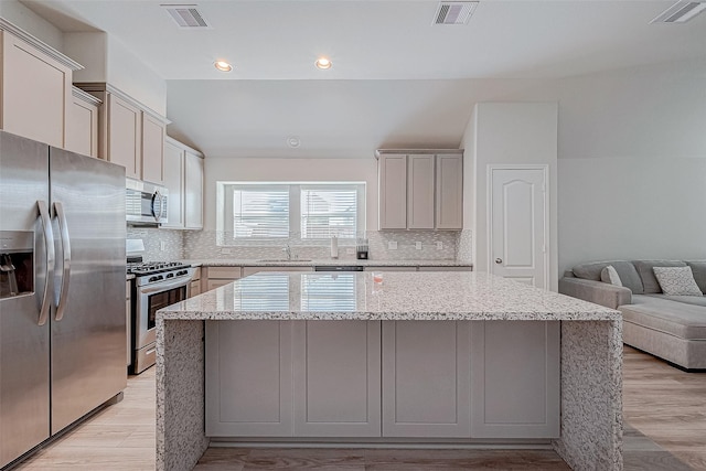 kitchen with a center island, stainless steel appliances, light hardwood / wood-style flooring, and tasteful backsplash