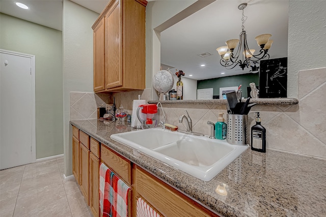 kitchen featuring light stone countertops, sink, an inviting chandelier, backsplash, and light tile patterned floors