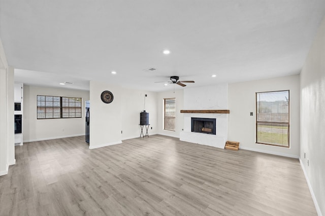 unfurnished living room with ceiling fan, a large fireplace, and light wood-type flooring