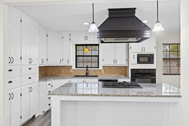 kitchen featuring custom exhaust hood, sink, black appliances, white cabinets, and hanging light fixtures