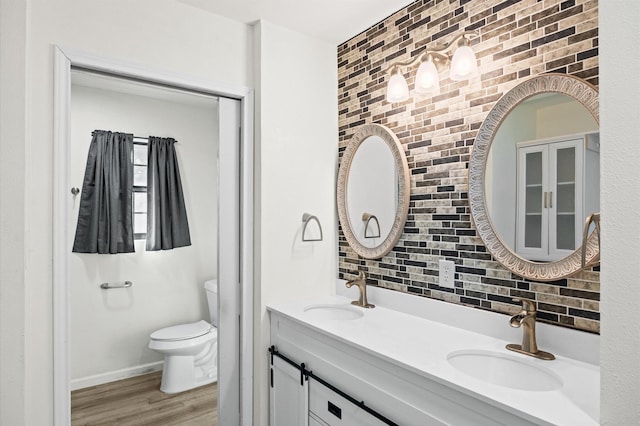 bathroom featuring hardwood / wood-style flooring, vanity, toilet, and brick wall