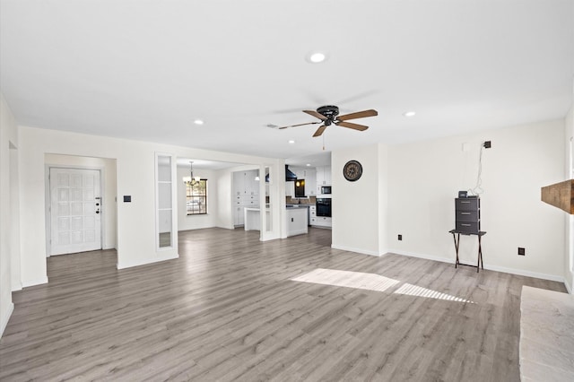 unfurnished living room featuring ceiling fan with notable chandelier and hardwood / wood-style flooring