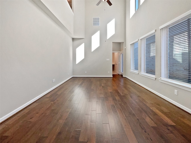 unfurnished living room with ceiling fan, dark hardwood / wood-style flooring, a high ceiling, and a wealth of natural light