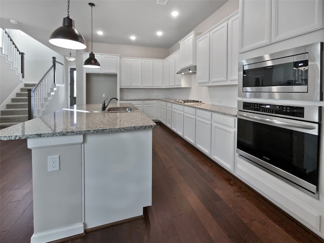 kitchen featuring a center island with sink, light stone countertops, dark hardwood / wood-style flooring, white cabinetry, and stainless steel appliances