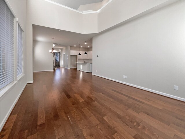 unfurnished living room featuring a chandelier, dark wood-type flooring, and a high ceiling