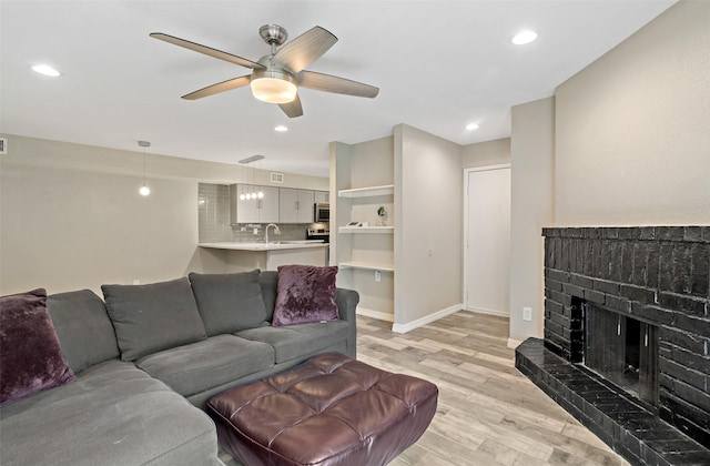 living room with a brick fireplace, light hardwood / wood-style flooring, ceiling fan, and sink