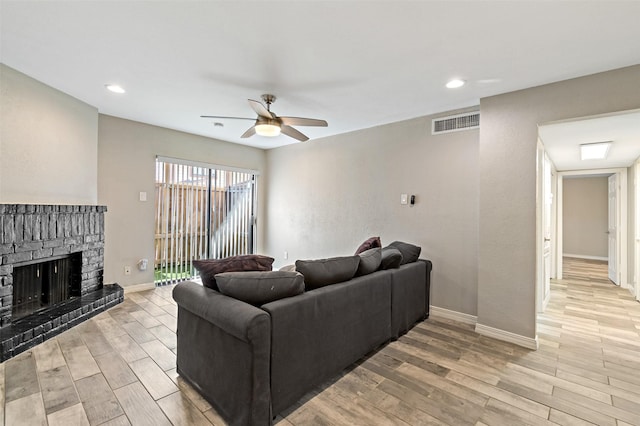 living room featuring visible vents, light wood-style flooring, a fireplace, and a ceiling fan