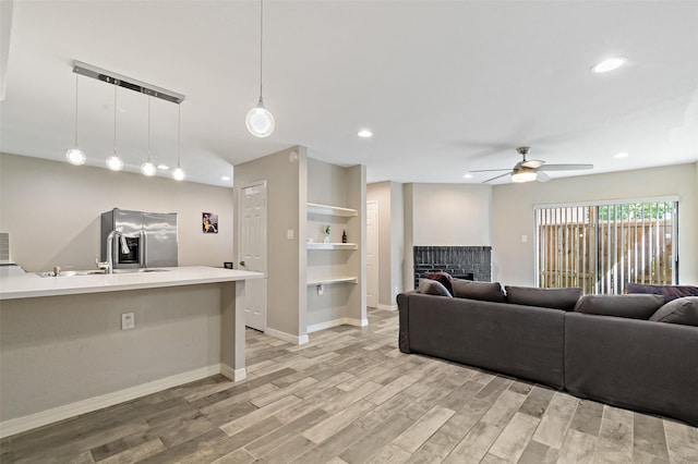 living room featuring a brick fireplace, light wood-type flooring, recessed lighting, and a ceiling fan
