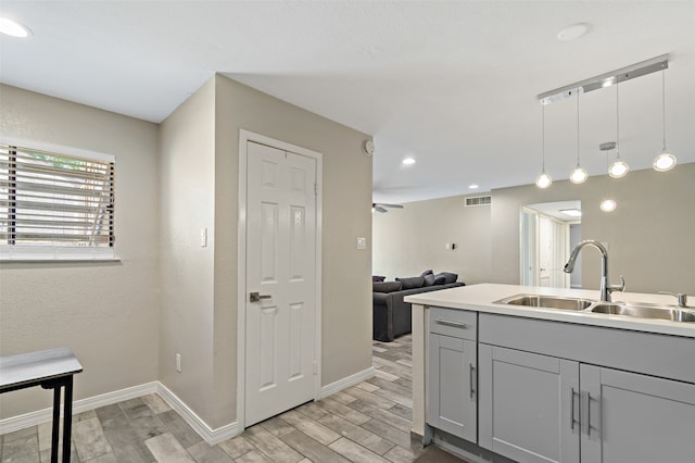 kitchen with ceiling fan, sink, light hardwood / wood-style flooring, gray cabinets, and hanging light fixtures