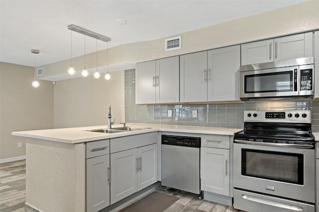 kitchen featuring kitchen peninsula, tasteful backsplash, stainless steel appliances, sink, and hanging light fixtures