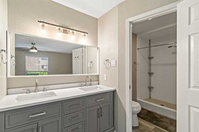 bathroom featuring vanity, ceiling fan, tiled shower, wood-type flooring, and toilet