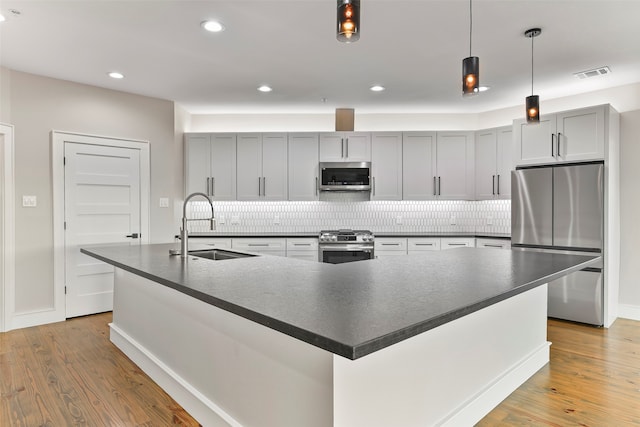 kitchen featuring a large island, sink, stainless steel appliances, tasteful backsplash, and light hardwood / wood-style flooring