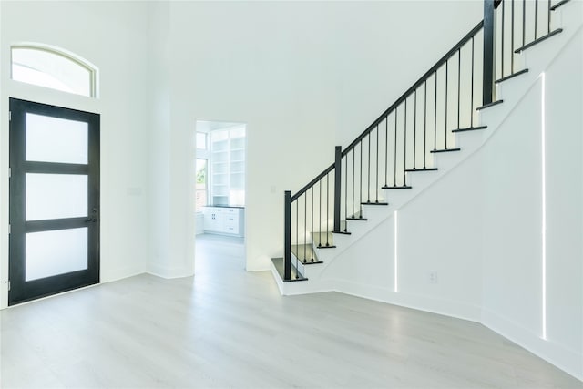 foyer entrance featuring light hardwood / wood-style floors, a healthy amount of sunlight, and a towering ceiling