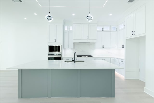 kitchen featuring hanging light fixtures, white cabinetry, a kitchen island with sink, and sink