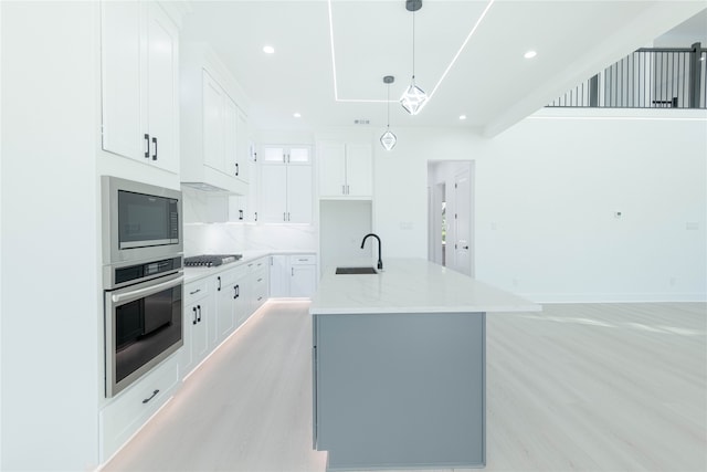 kitchen featuring light stone countertops, sink, stainless steel appliances, a kitchen island with sink, and white cabinets