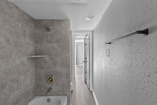 bathroom with a textured ceiling and tiled shower / bath