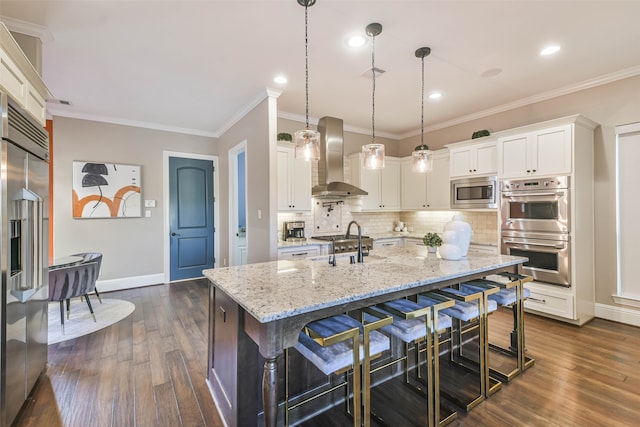 kitchen with dark wood-type flooring, a kitchen island with sink, white cabinets, built in appliances, and wall chimney exhaust hood