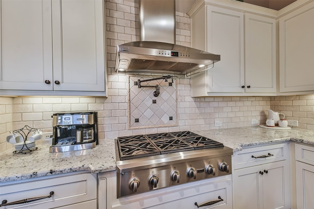 kitchen with light stone countertops, tasteful backsplash, wall chimney exhaust hood, white cabinetry, and stainless steel gas stovetop