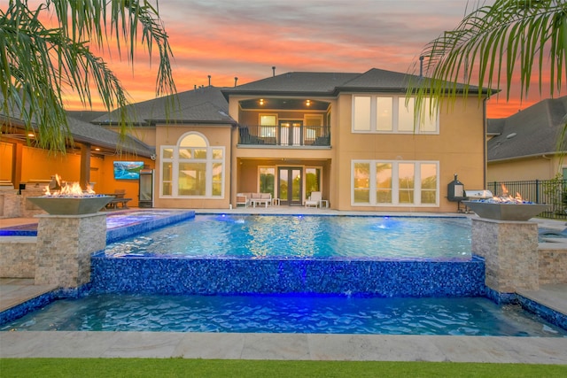 pool at dusk with pool water feature, a jacuzzi, and a patio